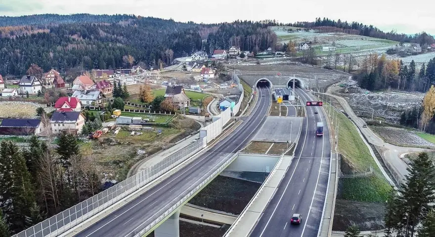 Nowa zakopianka trasa z tunelami i wiaduktami, otoczona lasami i zabudowaniami.