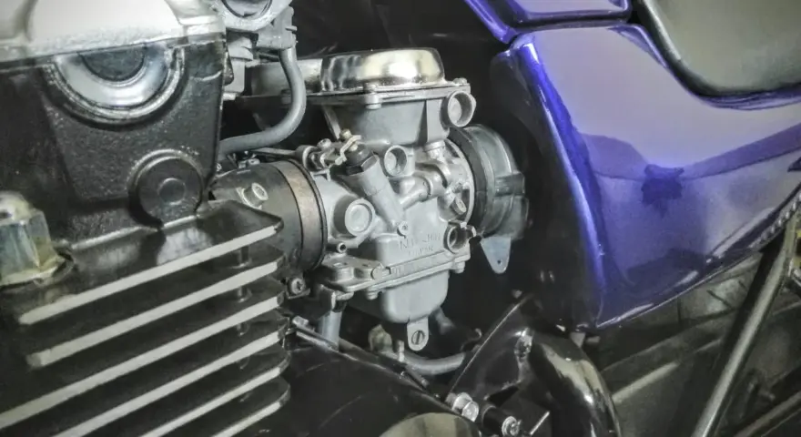Szczegółowy widok gaźnika motocyklowego, kluczowego elementu układu dolotowego, z widocznymi przewodami i częściami silnika.