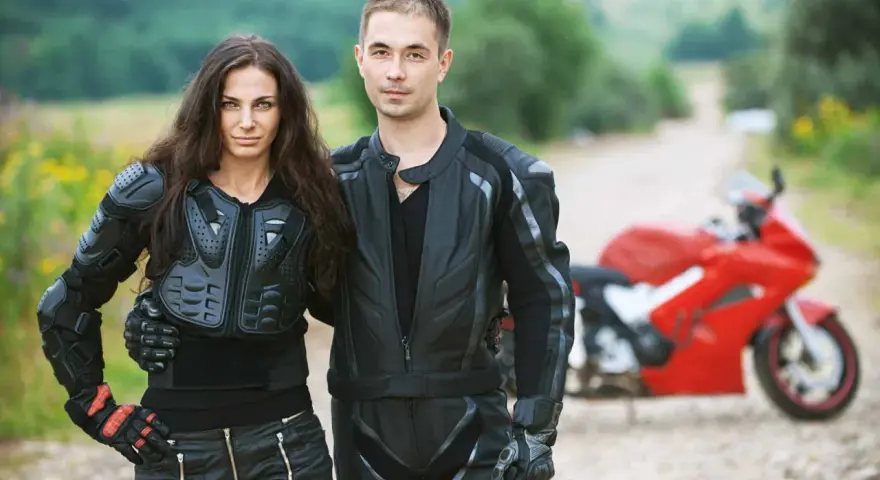 Para gotowa na jazdę na motorze. Ona w zbroi, on w skórzanej kurtce. Czerwony motocykl czeka.