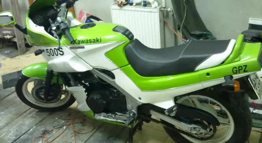 Zielono-biały motocykl Kawasaki GPZ 500 z napisem "GPZ" na tyle. Stoi na drewnianej podłodze w garażu.