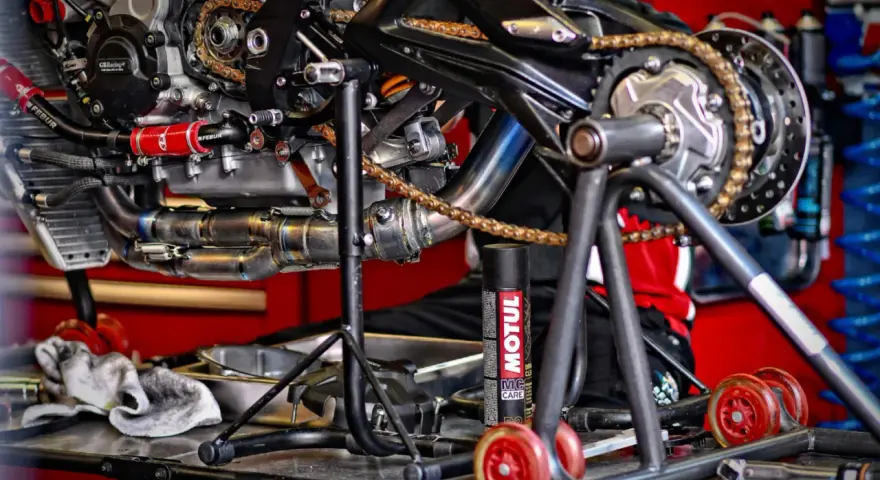 Motocykl na stojaku, widoczny napęd i łańcuch. Puszka smaru Motul sugeruje, co ile smarować łańcuch w motocyklu.