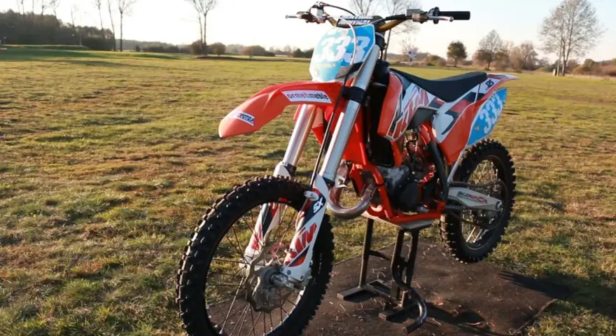 Pomarańczowy motocykl KTM SX 125 na stojaku, gotowy do jazdy. Zastanawiasz się, ile koni ma KTM SX 125? Ten model to potęga na torze!