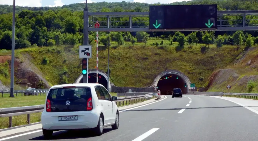 W Chorwacji są płatne autostrady. Biały samochód zbliża się do tunelu, sygnalizacja świetlna zielona.
