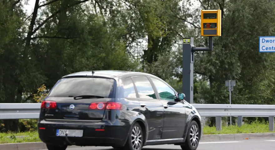 Czarny samochód mija fotoradar. Kierowca motocykla powinien uważać na ograniczenie prędkości.