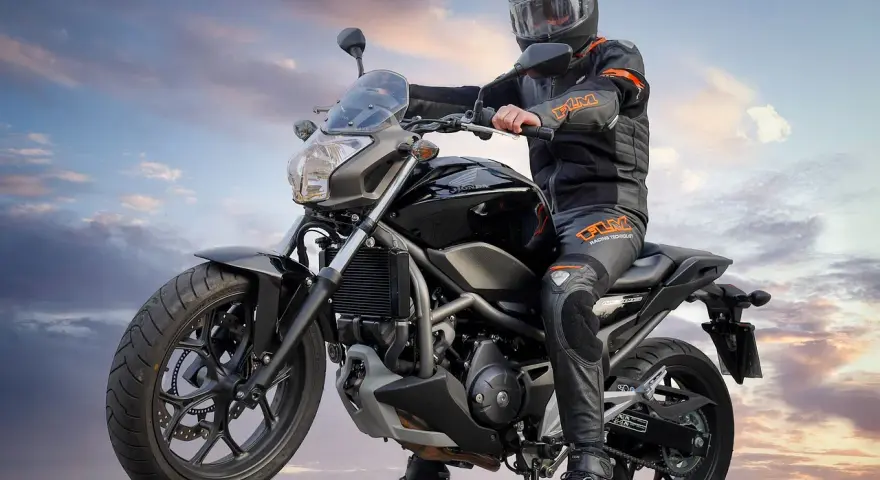 Motocyklista w kasku i kombinezonie siedzi na czarnym motocyklu. Idealny motor na kat B, gotowy na przygodę.