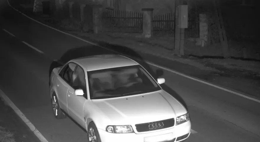Biały sedan Audi przejeżdża przez nocne zdjęcie z fotoradaru.