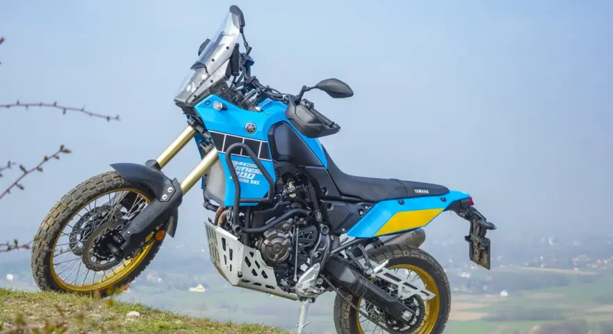 Niebiesko-żółty motocykl Yamaha Tenere 700 Rally gotowy na przygodę na wzgórzu.