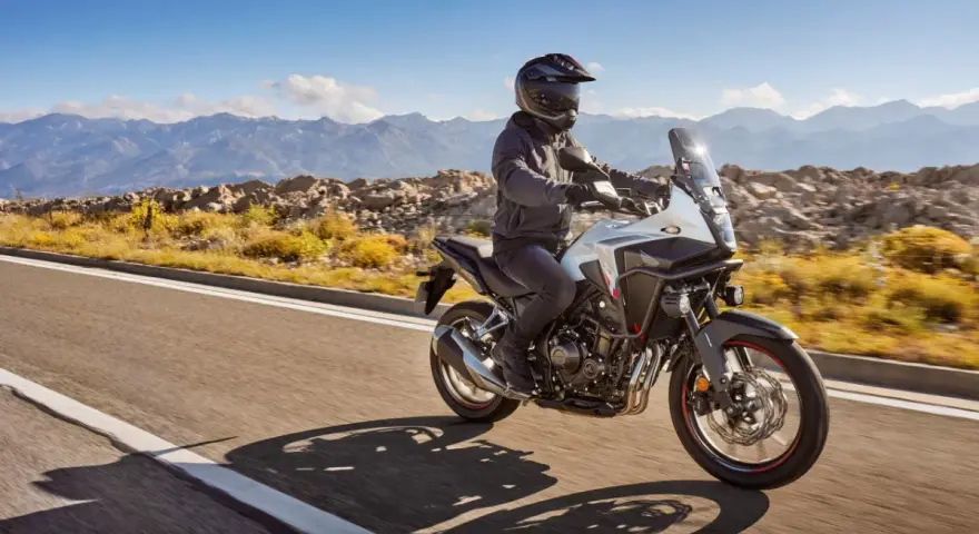Motocyklista na białym Honda CB500X przemierza malowniczą, górską drogę.