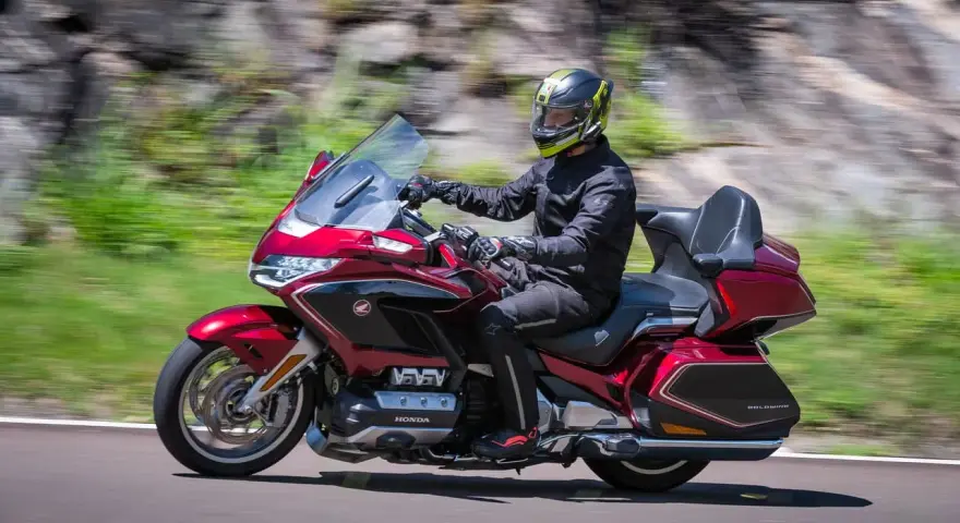 Mężczyzna w kasku jedzie lśniącym, czerwonym motocyklem Honda Gold Wing, uznawanym za najlepszy motocykl turystyczny.