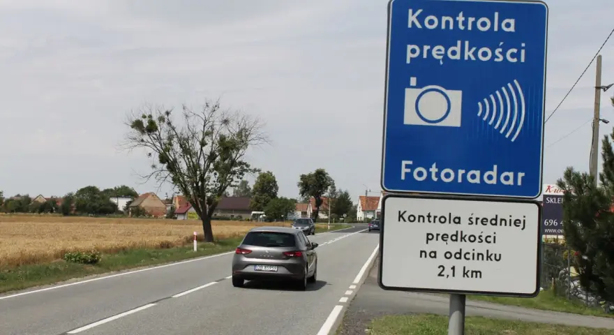 Znak "Kontrola prędkości Fotoradar" informuje, że czy fotoradar musi być oznakowany. Obok droga i pola.