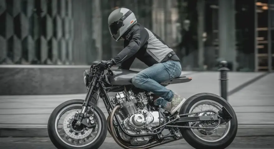 Motocyklista w kasku i jeansach pędzi na stylowym Suzuki GS 650 po miejskiej ulicy.