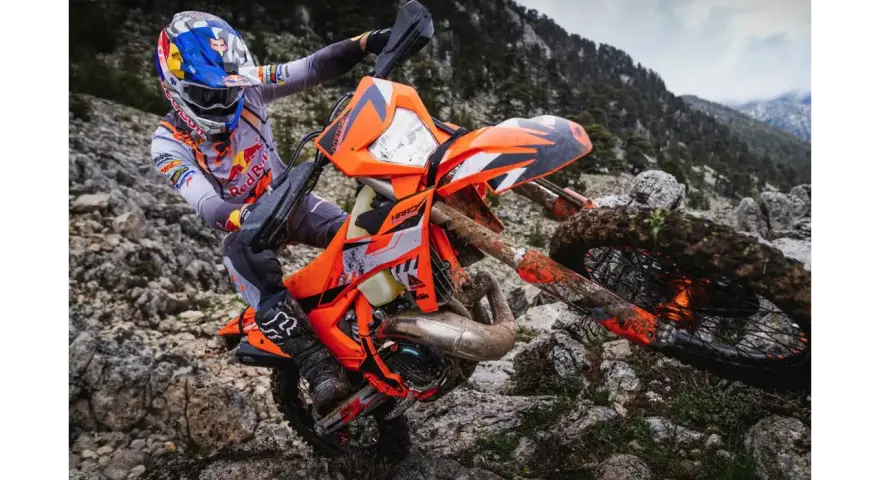 Motocyklista w kasku Red Bull na pomarańczowym KTM EXC 300 2T pokonuje kamienisty teren. Dane techniczne tego potwora terenowego są imponujące.
