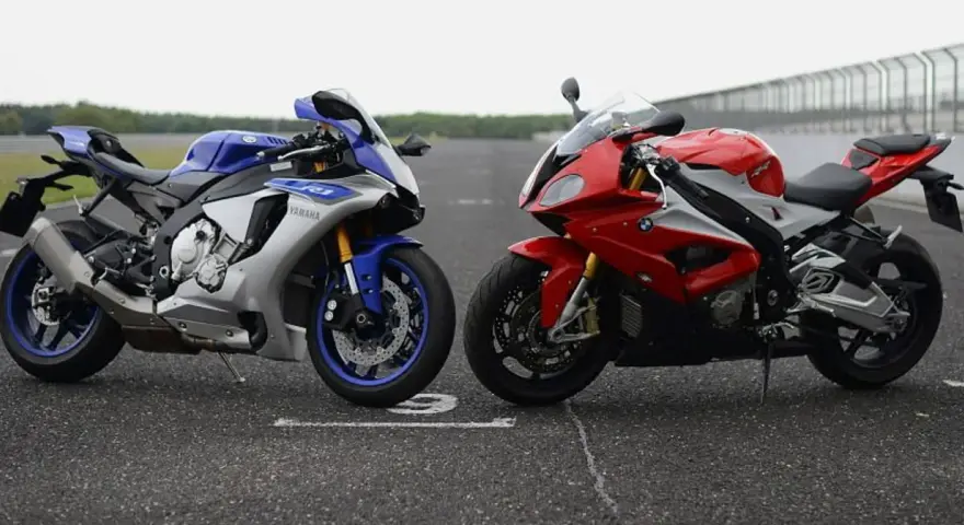 Dwa sportowe motocykle: niebiesko-srebrny Yamaha R1 i czerwono-biały BMW S1000RR 2020, stojące na torze wyścigowym.