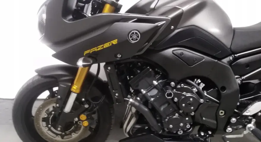 Ciemnoszary motocykl Yamaha FZ8 z żółtym napisem "FAZER" na baku. Widoczny fragment przedniego koła, zawieszenia i silnika.