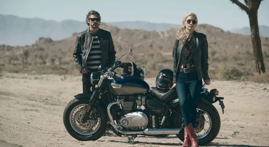 Para w skórzanych kurtkach pozuje przy motocyklu Triumph Speedmaster na pustynnym tle.