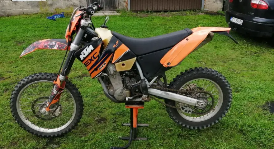 Pomarańczowy motocykl KTM 400 EXC na stojaku, gotowy do jazdy po bezdrożach.