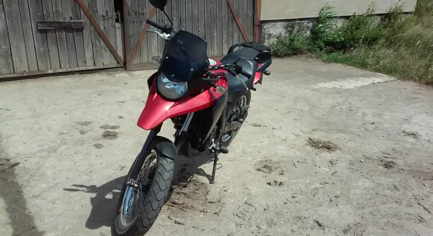 Czerwony motocykl Derbi Terra 125 stoi przed drewnianą stodołą.