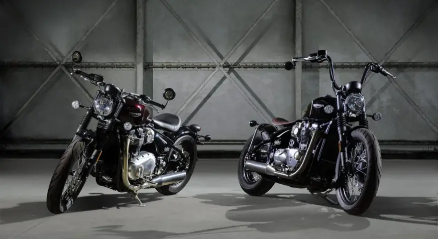 Dwa motocykle Triumph Bonneville Bobber w ciemnych kolorach, stojące obok siebie w industrialnym wnętrzu.