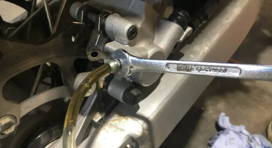 Klucz nasadowy odkręca odpowietrznik podczas czyszczenia hamulców motocykla. Płyn hamulcowy spływa przez przezroczysty wężyk.