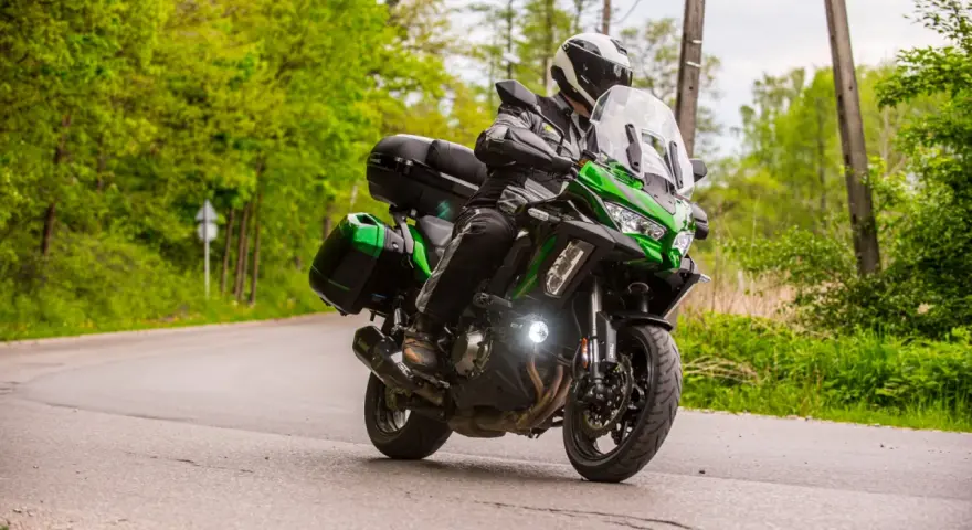 Motocyklista na zielonym Kawasaki Versys 1000, z kuframi, pokonuje zakręt. Nawet z potencjalnymi wadami, jazda nim to przygoda.