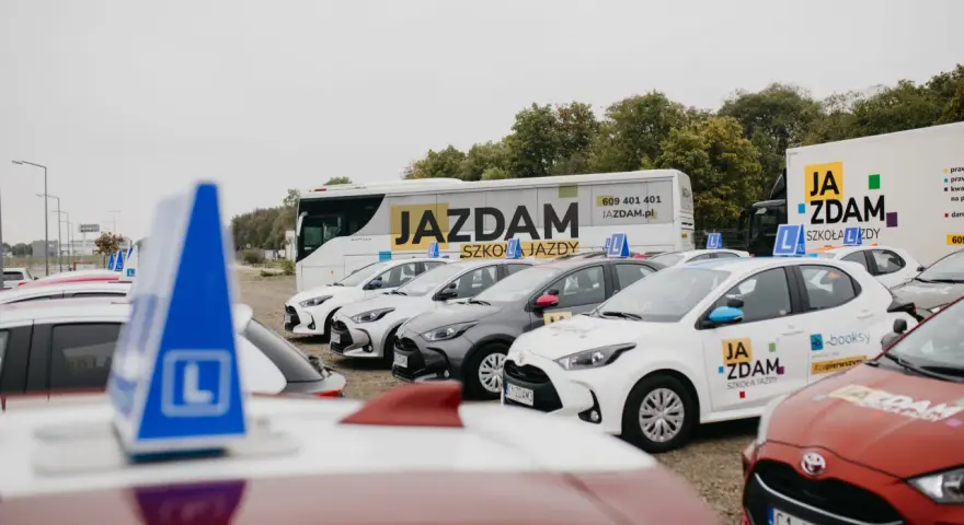 Auta szkoleniowe z literą "L" na dachu, gotowe do nauki różnych kategorii prawa jazdy.