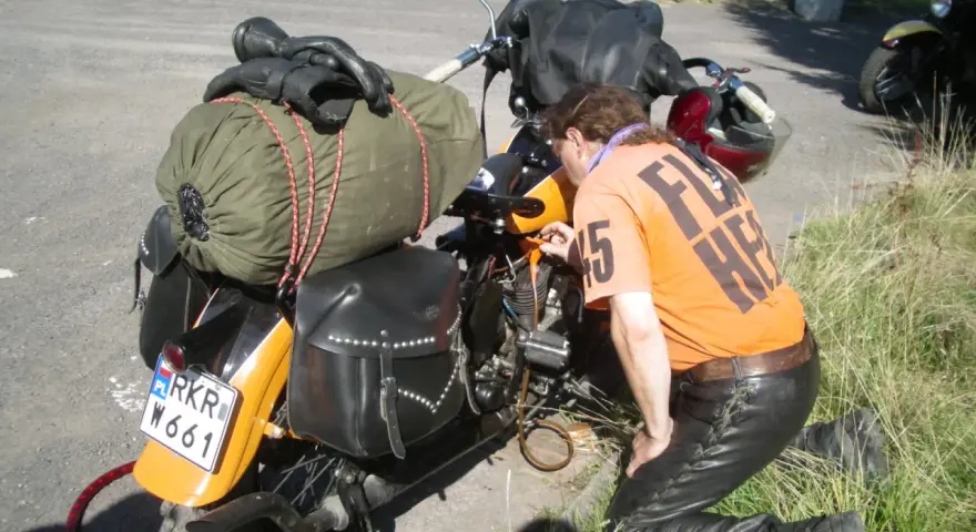Motocyklista sprawdza uszkodzony gaźnik objawy. Na motocyklu sakwy, zielony worek i czarne rękawice.