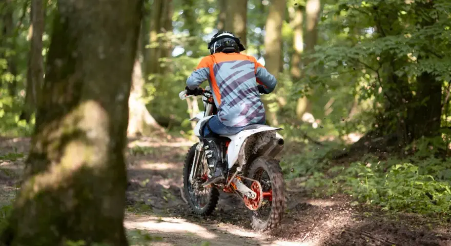 Motocyklista w kasku i kolorowej bluzie pędzi leśnym szlakiem. Od ilu lat można jeździć crossem? Odpowiedź zależy od przepisów i umiejętności.