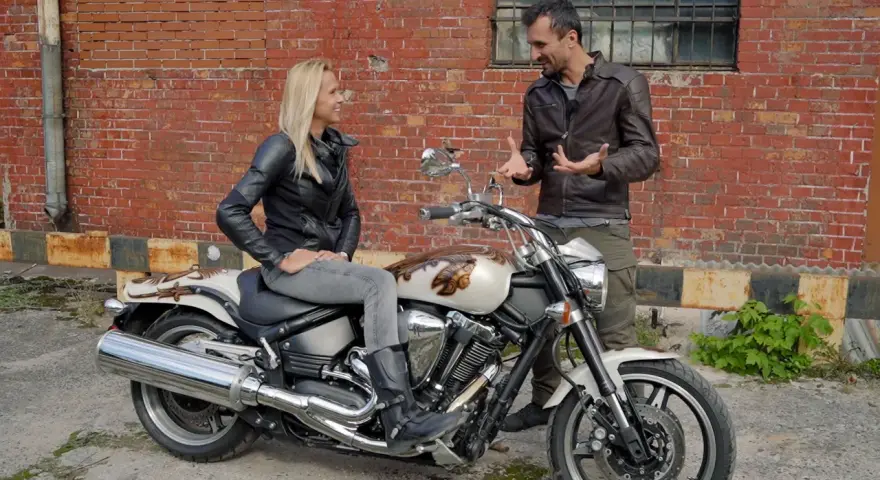 Kobieta siedzi na motocyklu Yamaha Warrior 1700, mężczyzna obok opowiada o jego możliwościach.