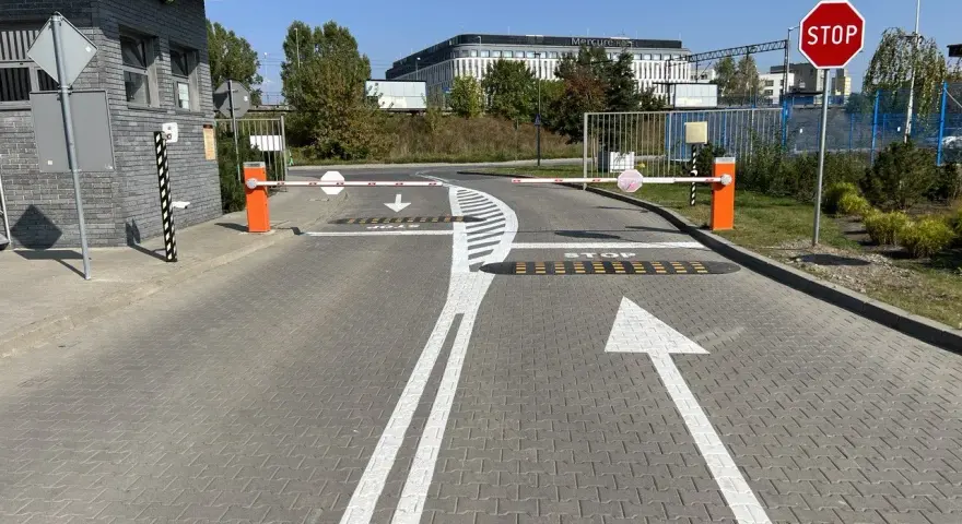 Przed wjazdem na teren, gdzie obowiązuje znak P-15, stoją szlabany. Na drodze namalowano strzałki kierunkowe i napis STOP.