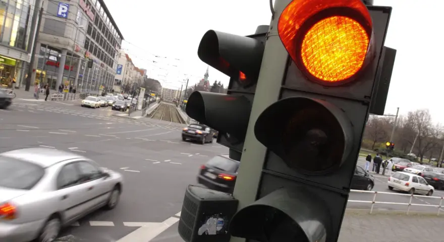 Żółte światło na sygnalizatorze drogowym, ruch uliczny i budynki w tle.