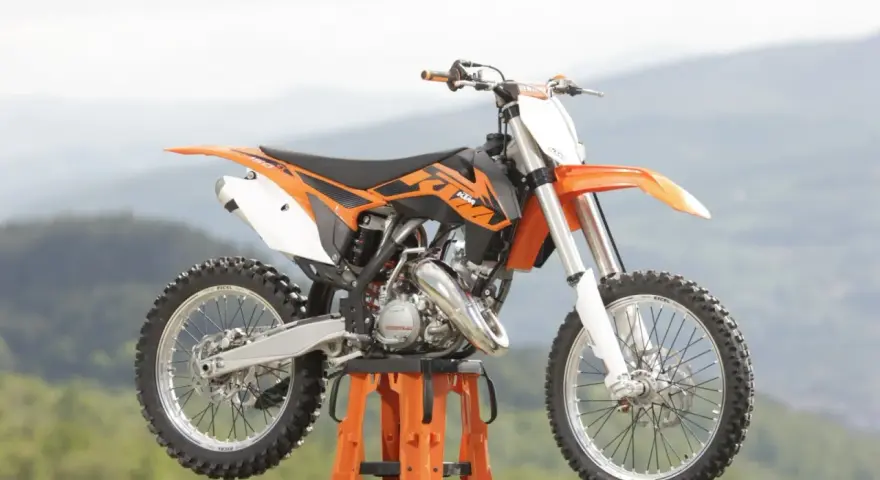 Pomarańczowy KTM SX 125 gotowy do osiągnięcia v-max na górskich trasach.