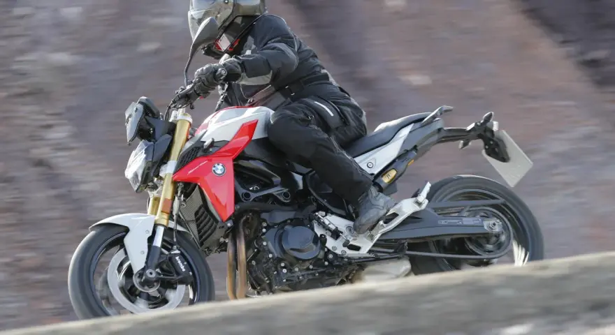 Motocyklista w kasku i kombinezonie pędzi na motocyklu BMW F900R po kamienistym terenie.