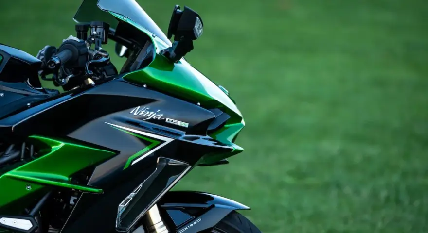 Błyszczący, czarno-zielony motocykl Kawasaki H2 SX z napisem "Ninja H2 SX" na owiewce, zaparkowany na tle zielonej trawy.