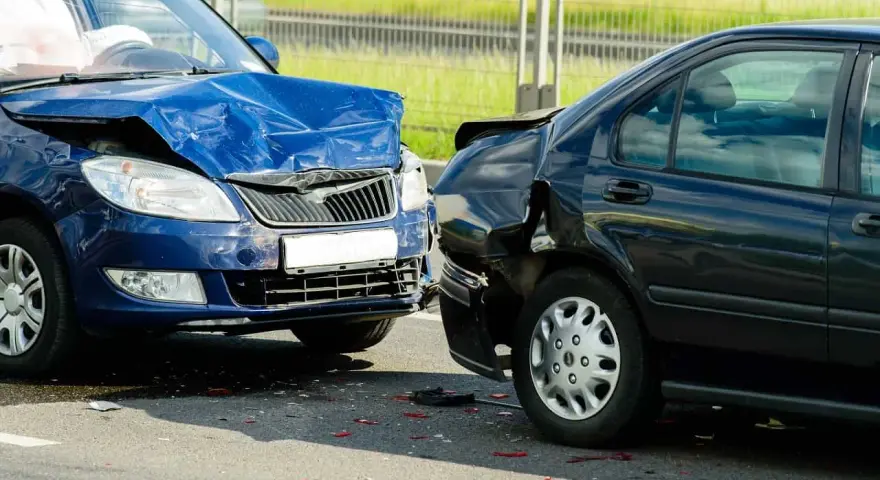 Dwa uszkodzone samochody po kolizji. Niebieski przód jest mocno zgnieciony, a czarny tył również nosi ślady uderzenia. Prawdopodobnie czeka ich mandat za kolizje.