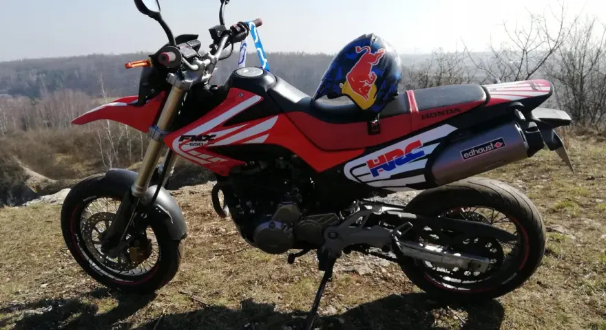 Czerwony motocykl Honda FMX 650 z kaskiem Red Bull na siedzeniu, gotowy na przygodę w terenie.