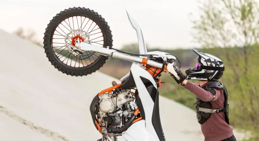 Motocyklista w kasku i ochraniaczach wykonuje wheelie na piaskowej wydmie. To najszybszy cross na świecie, gotowy do akcji.