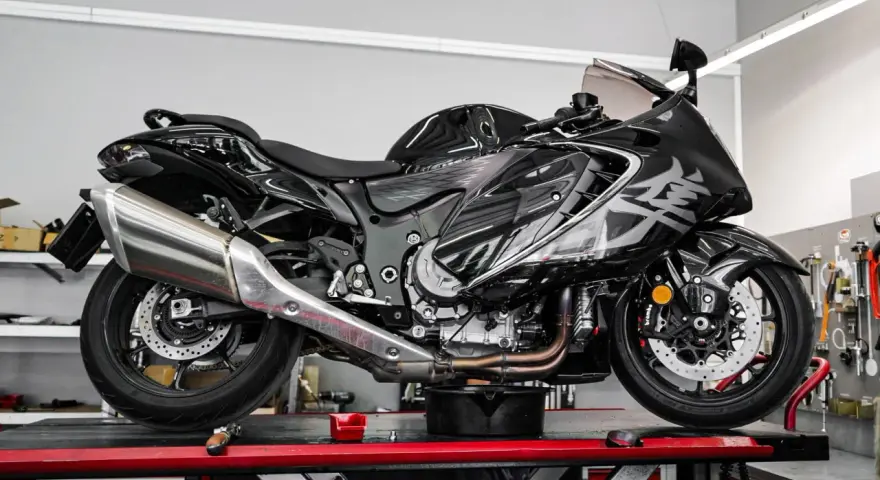 Czarny motocykl na podnośniku, gotowy do serwisu. Widać duży, chromowany wydech, który odcina się od reszty maszyny.