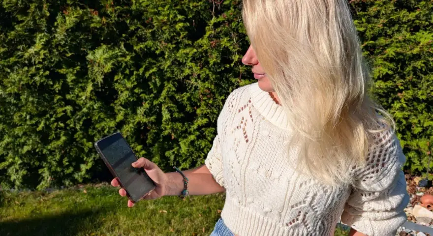 Blondynka w białym swetrze korzysta z telefonu, by wyznaczyć trasę krok po kroku.