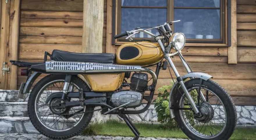 Żółty motorower WSK 175, z widocznymi danymi technicznymi na silniku, stoi przed drewnianym domem.