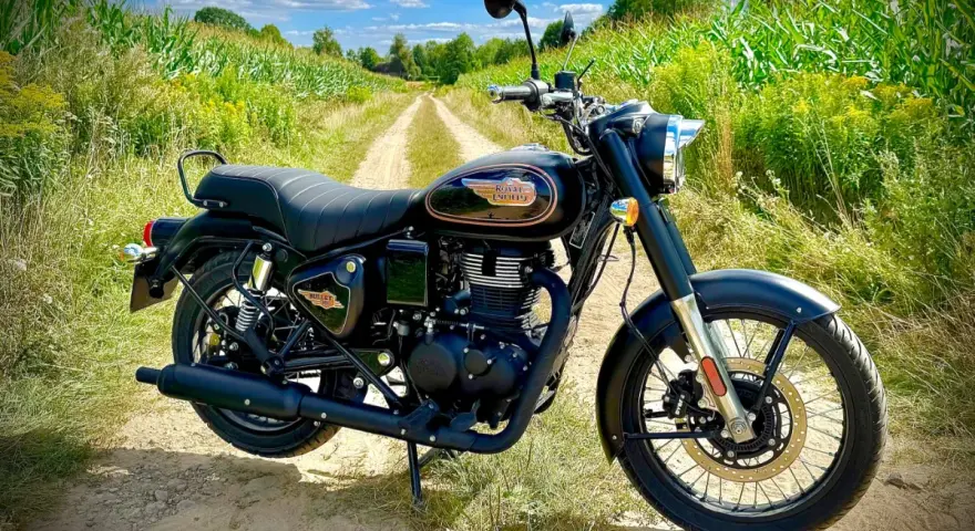 Czarny motocykl Royal Enfield Diesel na polnej drodze, otoczony zielenią i kukurydzą.