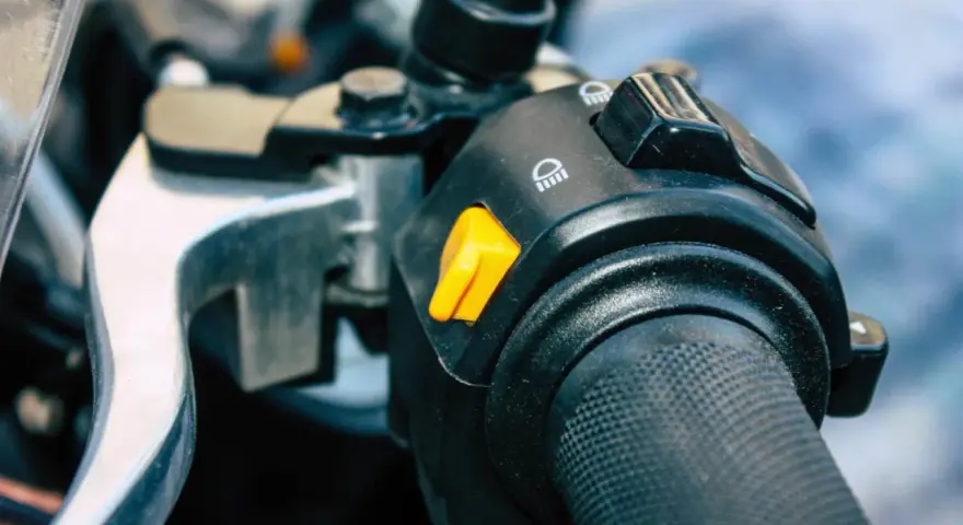 Pomarańczowy przycisk na kierownicy motocykla, który może służyć jako kill switch, obok przełącznika świateł.