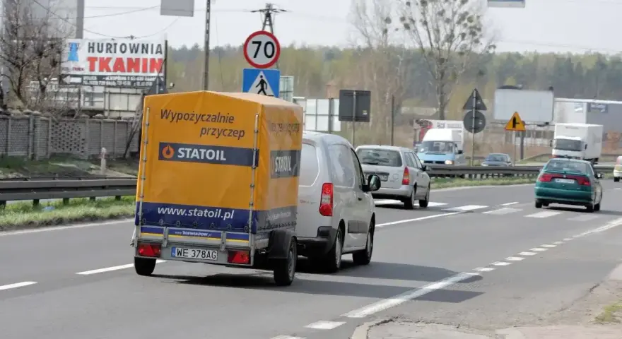 Samochód z przyczepą Statoil jedzie drogą. Znak ograniczenia prędkości 70 km/h sugeruje, ile można jechać na autostradzie w tym miejscu.