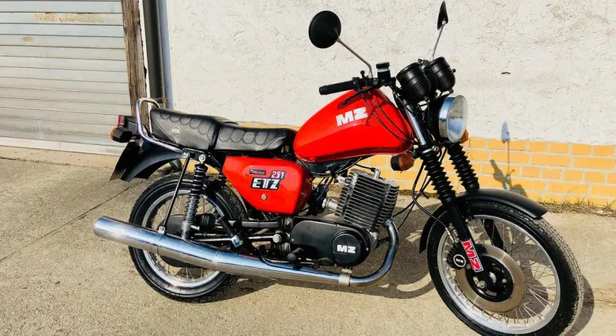 Czerwony motocykl MZ ETZ 251 z lat 80. stoi przed garażem.