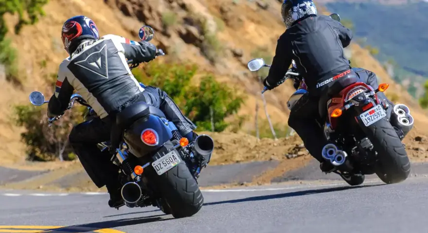 Dwóch motocyklistów na zakręcie. Jeden na Yamaha R3, drugi na V-Max, w skórzanych kombinezonach, pokonuje górską drogę.