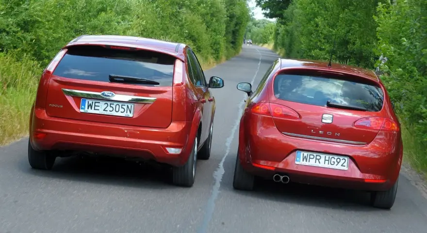 Dwa czerwone auta jadą drogą. Jedno z nich, Ford Focus, próbuje omijanie, podczas gdy Seat Leon wykonuje wymijanie.