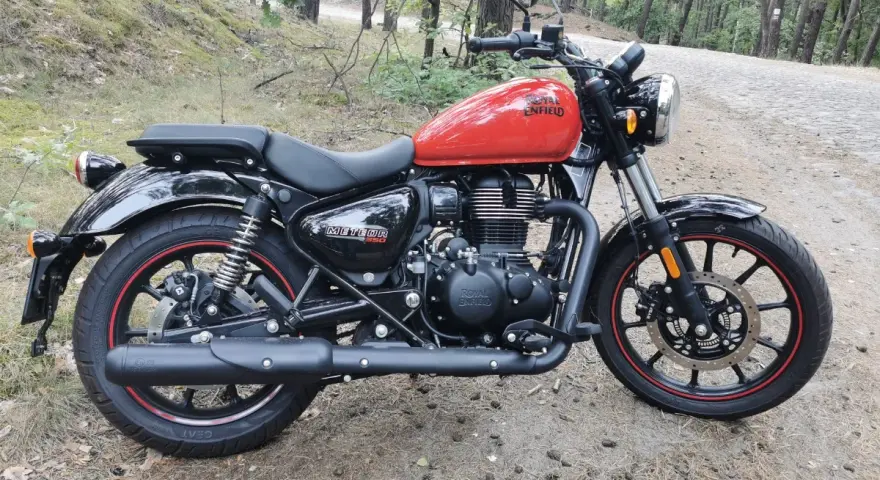 Czerwony Royal Enfield Meteor 350 na leśnej drodze. Klasyczny wygląd i gotowość do podróży.