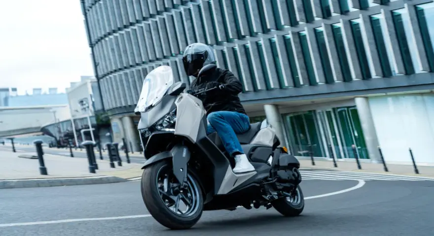Mężczyzna w kasku jedzie skuterem Yamaha X-MAX 125 po mieście. Czy to lepszy wybór niż Honda Forza 125?