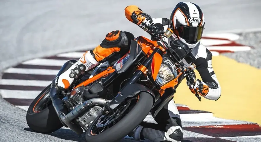 Motocyklista w kombinezonie ściga się na torze na pomarańczowym KTM 1290 Super Duke, pochylony w zakręcie.