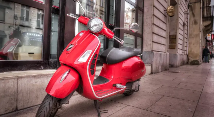 Czerwony skuter Vespa, idealny do miasta. Marzenie o posiadaniu go jest jak marzenie o zdobyciu prawa jazdy na skuter.