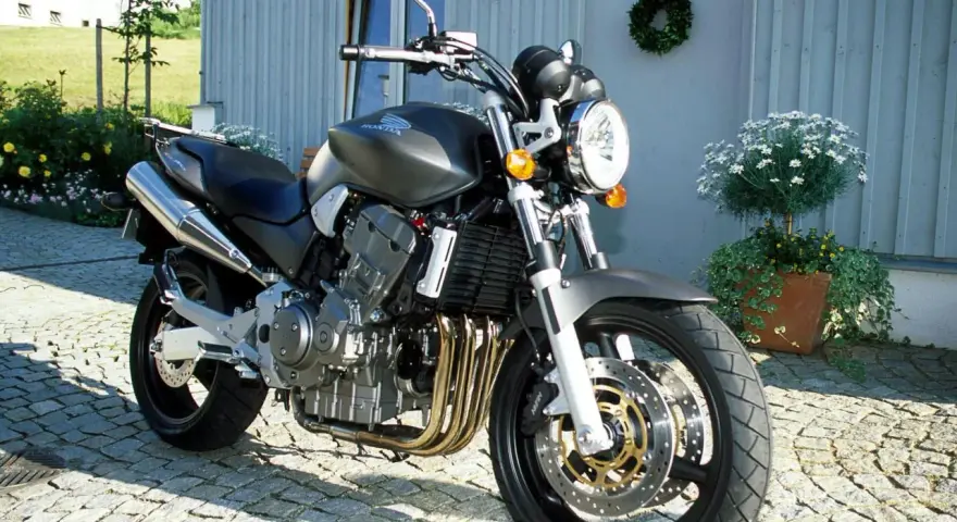 Szary motocykl Honda 919 zaparkowany na bruku przed domem.